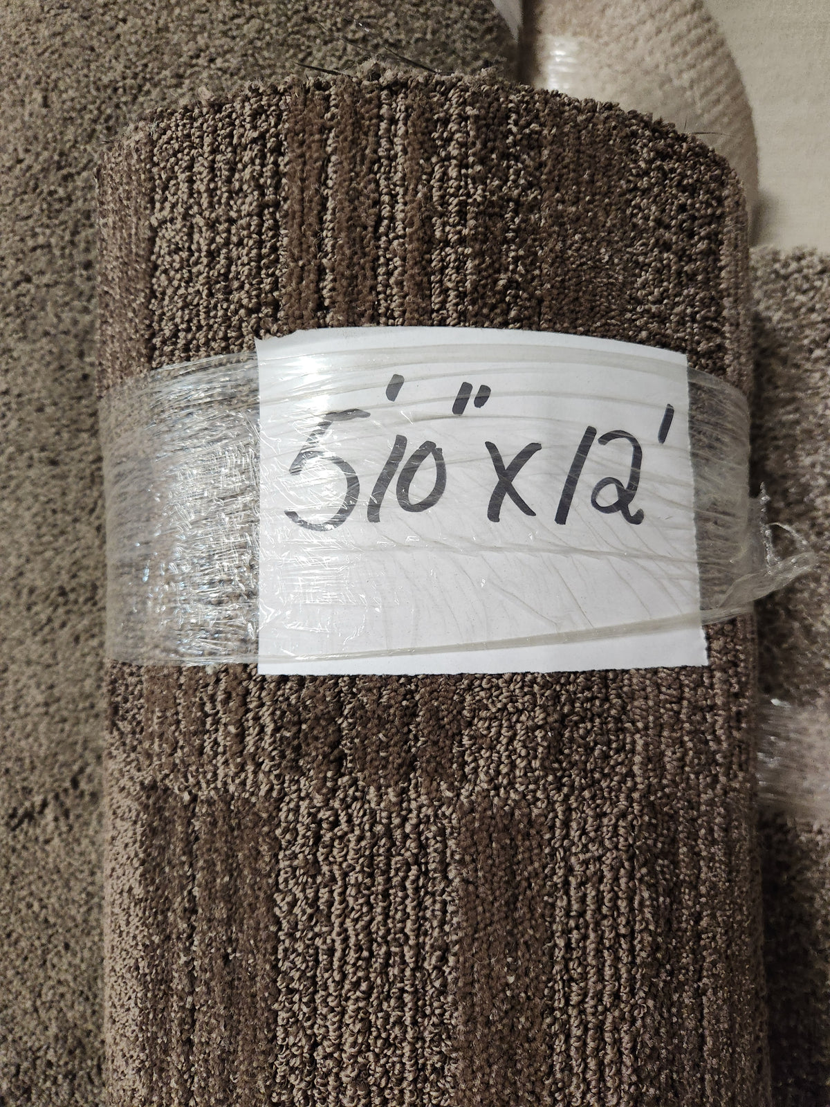 A low pile, dark brown Flooring CLEARANCE Carpet Remnant 5'10" x 12', rolled up in clear plastic.