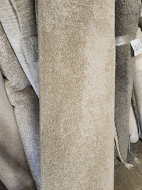 Several Flooring CLEARANCE Carpet Remnant 8'6" X 9' rolls in beige and grey are stacked vertically with a price tag.