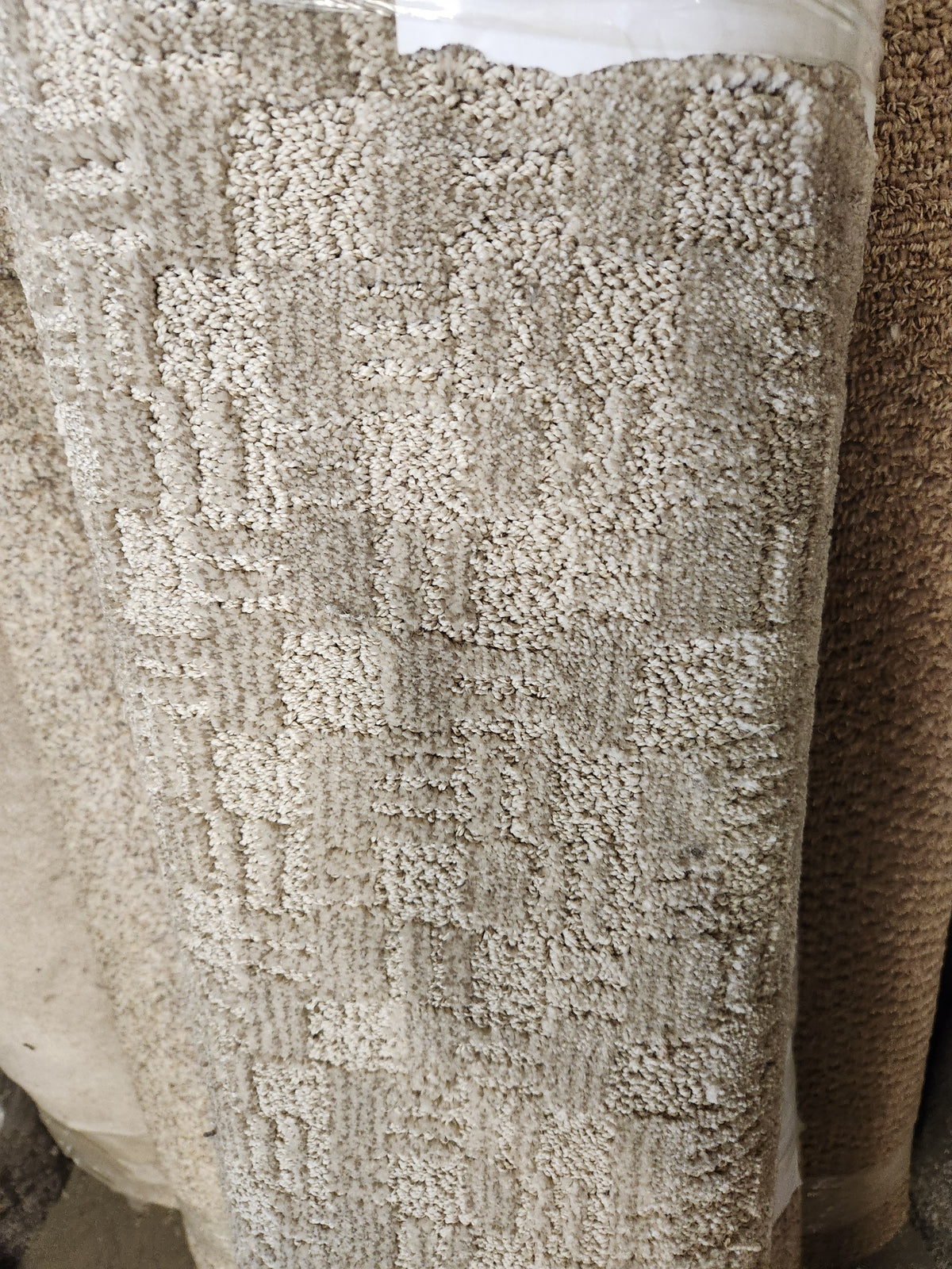 A 12" x 4'6" beige textured medium pile Carpet Remnant by Flooring CLEARANCE with a subtle square pattern.