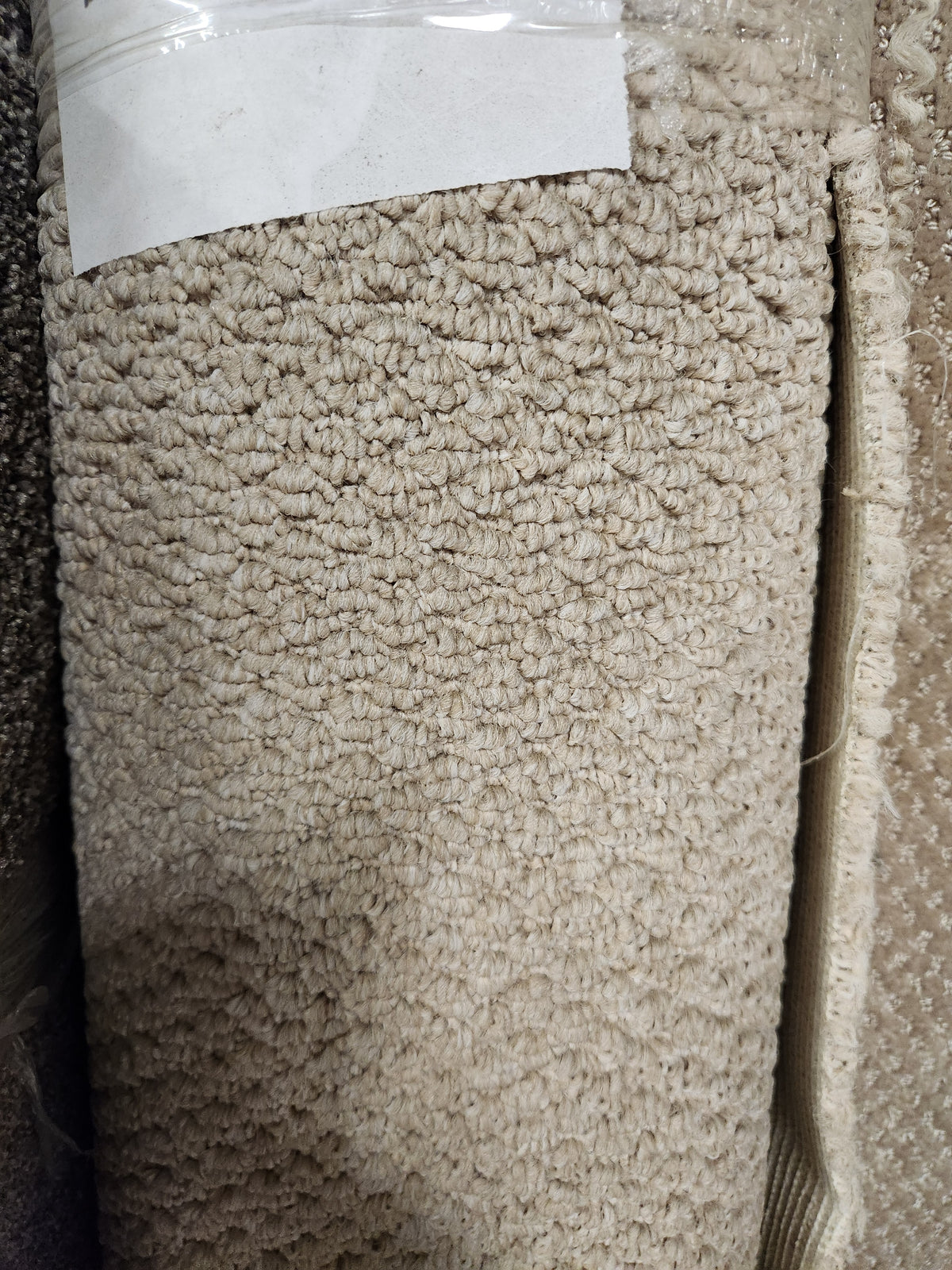 Close-up of Flooring CLEARANCE Carpet Remnant 4'10" X 7'5", looped beige roll with blank white label on top.