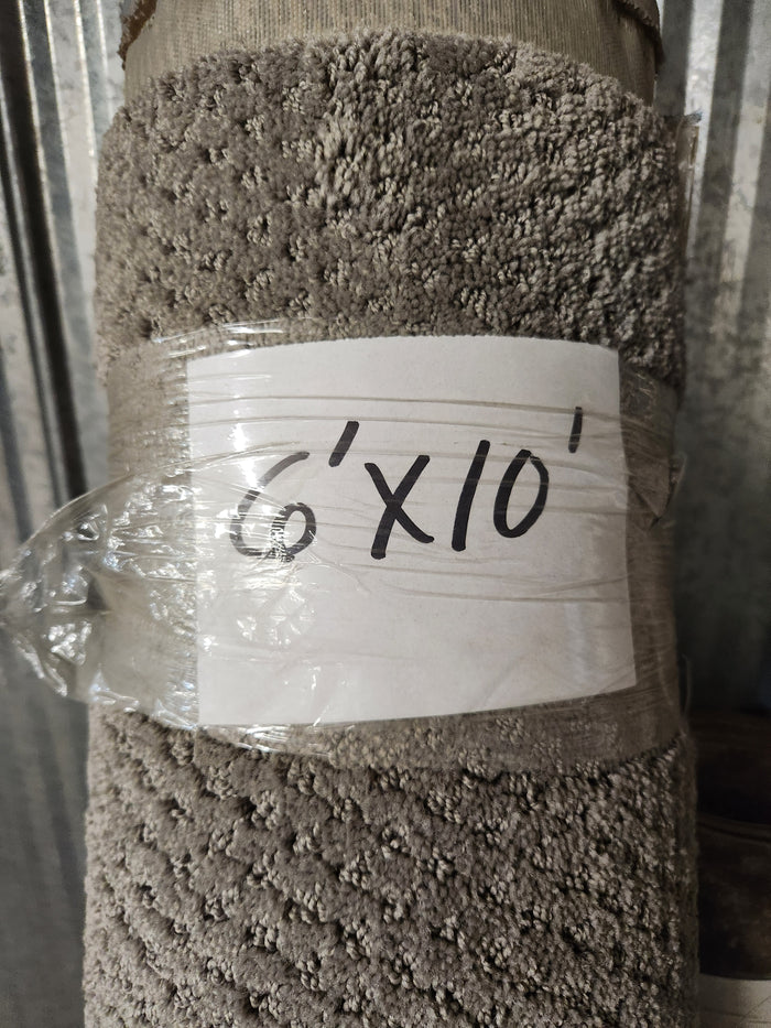 A Carpet Remnant 6' X 10' by Flooring CLEARANCE, beige with a looped pattern, rolled and wrapped in plastic.