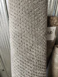 A Flooring CLEARANCE Carpet Remnant 6' X 10' in grey stands upright by another roll near a corrugated metal wall.