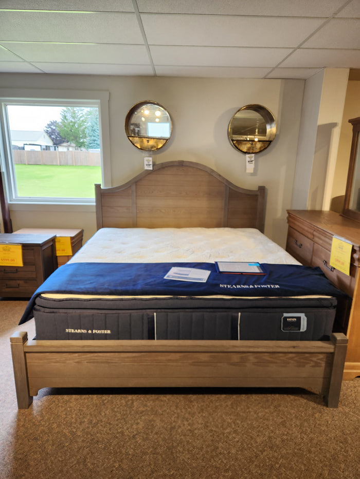 A showroom displays the Vaughan Bassett 740 Bungalow Arch King Bed with blue topper, nightstands, and round mirrors.