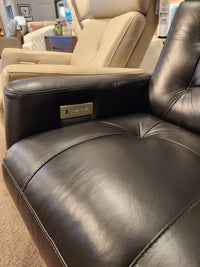 Close-up of a black Palliser recliner armrest with controls, next to a beige 43411 Baltic 2 Power Swivel Glider in a showroom.