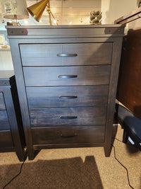 The Handstone Chattanooga 5 Drawer Highboy features dark wood and custom metal hardware, shown on a carpeted floor.