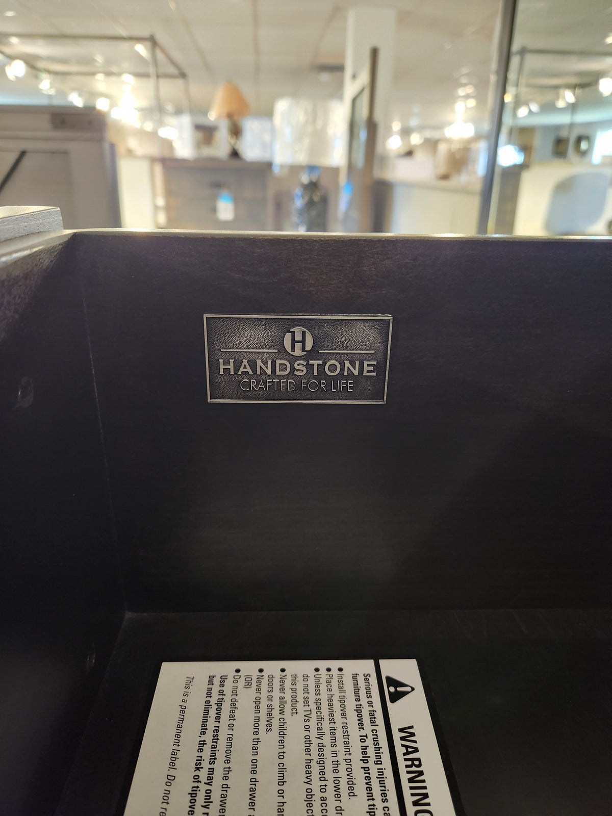 A metal "Handstone Crafted for Life" label is inside a Chattanooga 5 Drawer Highboy in a showroom.