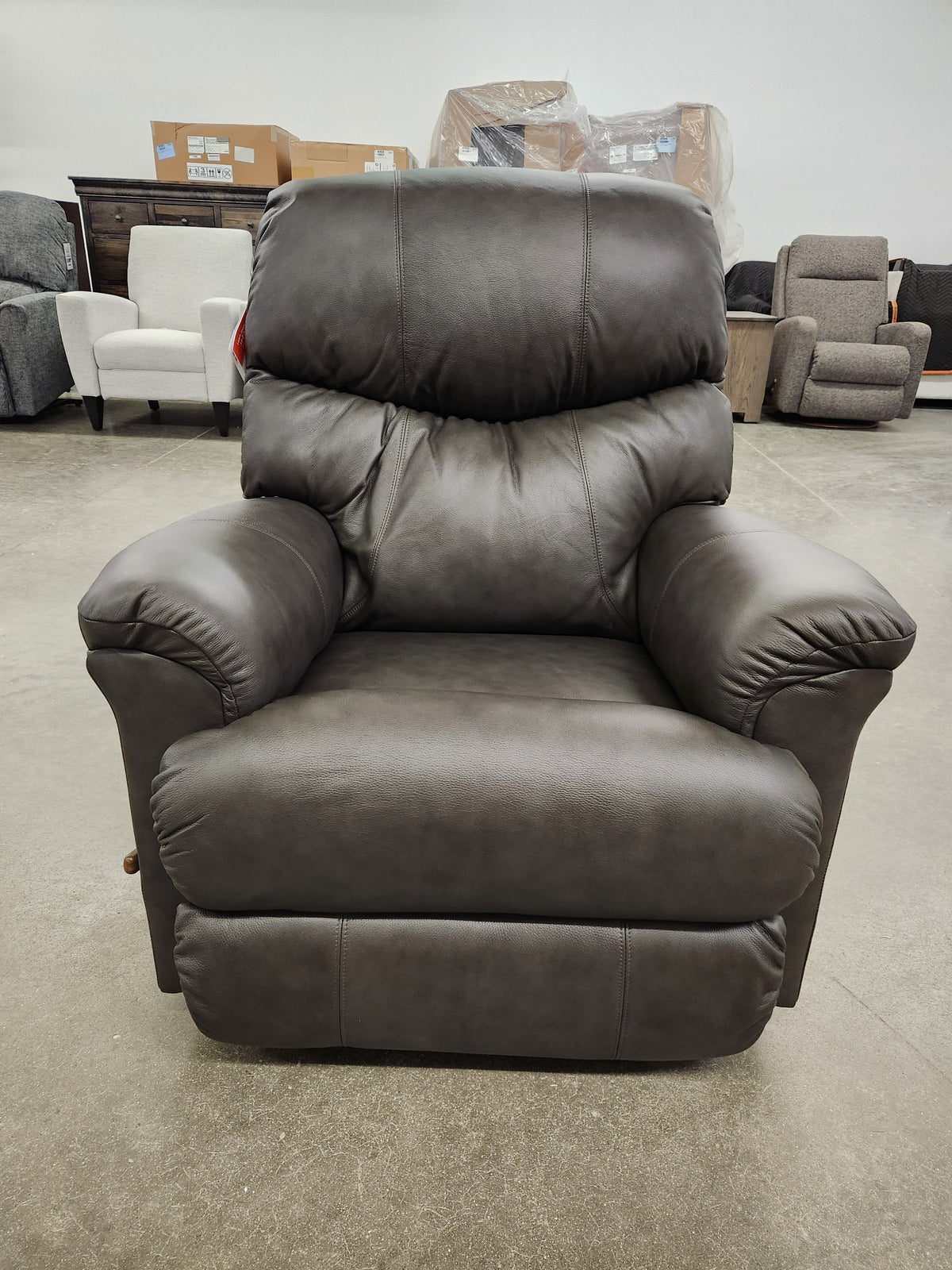 A dark brown La-Z-Boy 528 Larson All Leather Rocker Recliner with a chaise seat sits in a showroom with other chairs.