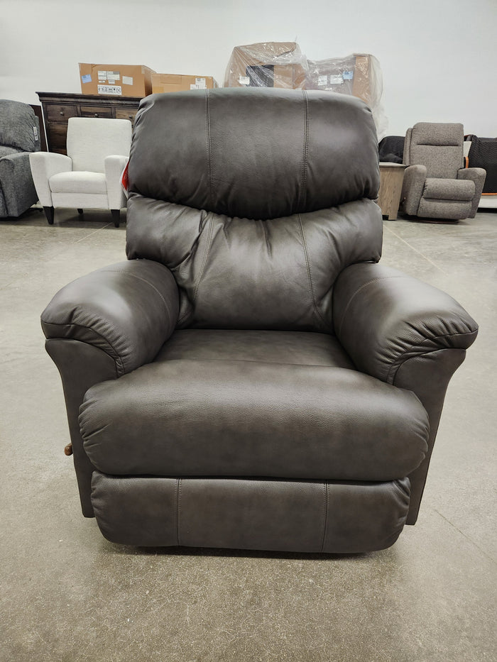 A dark brown La-Z-Boy 528 Larson All Leather Rocker Recliner with a chaise seat sits in a showroom with other chairs.