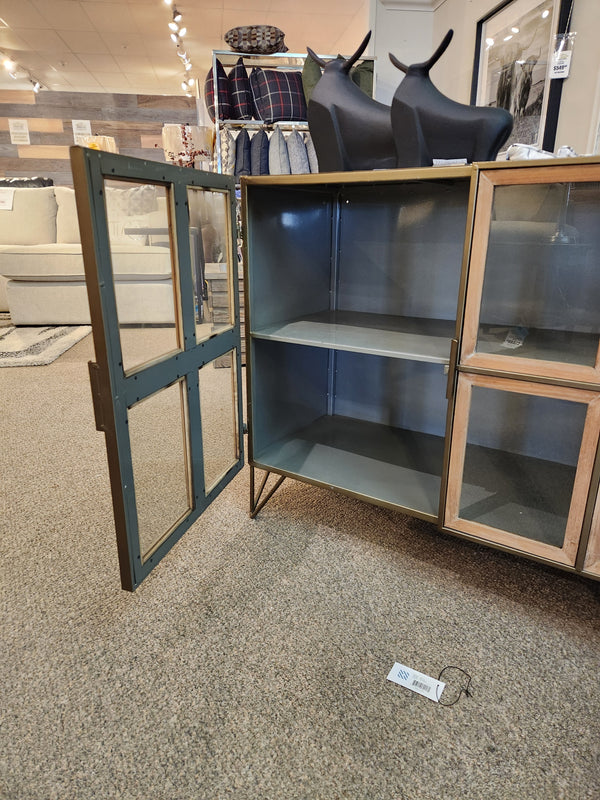 The Mercana Pandora Accent Cabinet with one door open reveals two empty shelves on a carpeted store floor.