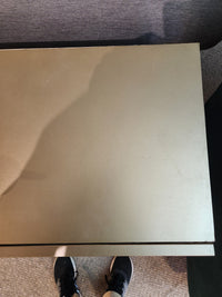 A person in black sneakers stands before a closed Mercana Pandora Accent Cabinet with an olive metal finish.