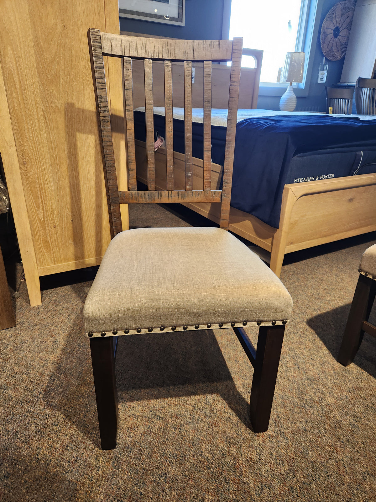 Jofran Willow Creek Slatback Chair with upholstered seat and studded trim, shown on a carpeted showroom floor.