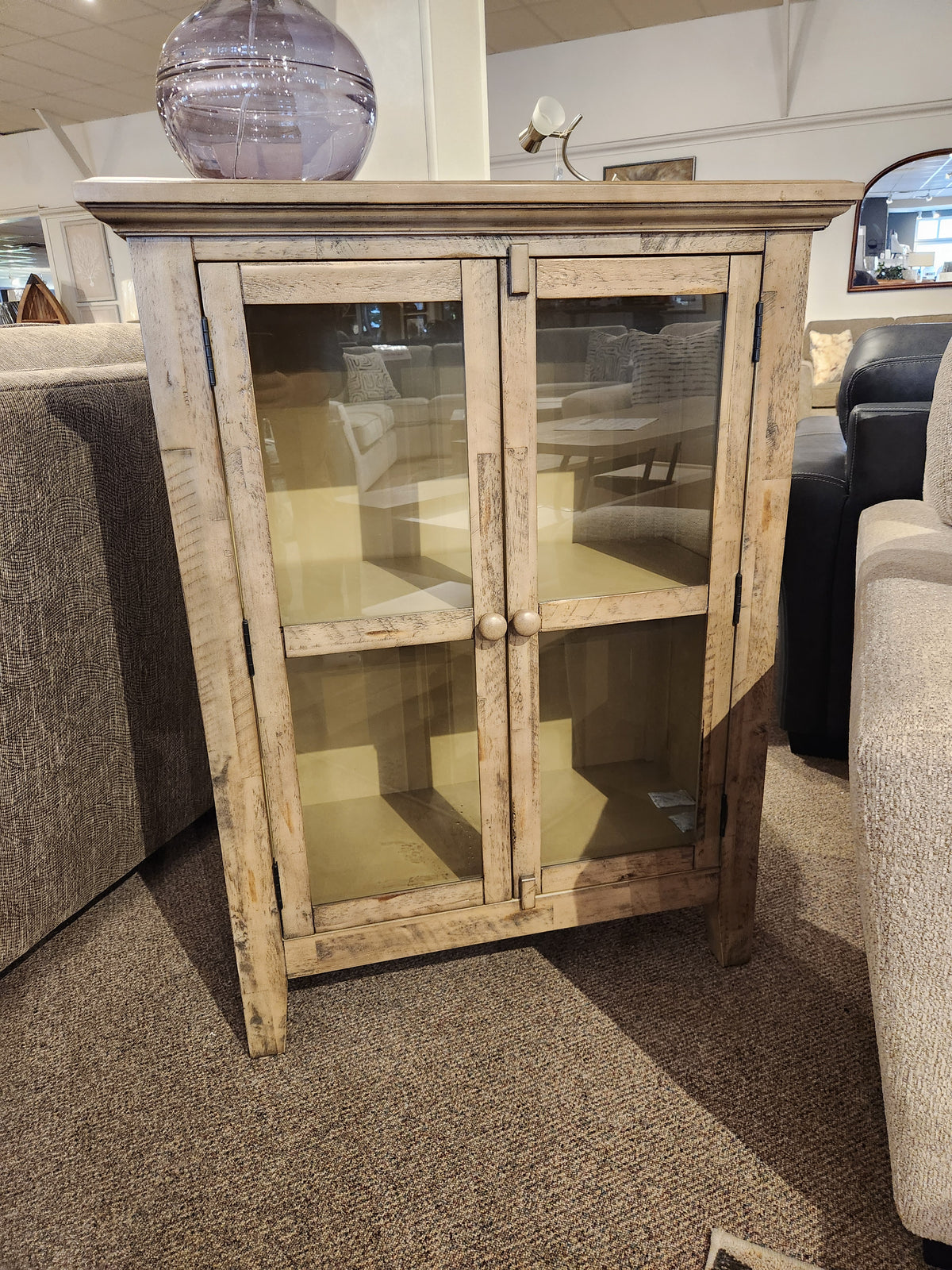 The Jofran Rustic Shores 2 Door Accent Cabinet with glass doors and two shelves sits between two sofas.