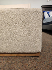 Close-up of the Nala Bed by Fashion: a cream boucle platform bed with wood base on brown carpet.