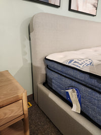 Close-up of a Palliser EQ3 Nara Queen Bedframe with modern headboard, blue mattress, and wood nightstand on carpet.