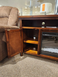 Jofran Urban Icon Electric Fireplace Media Console features open shelving for media storage beside a recliner.