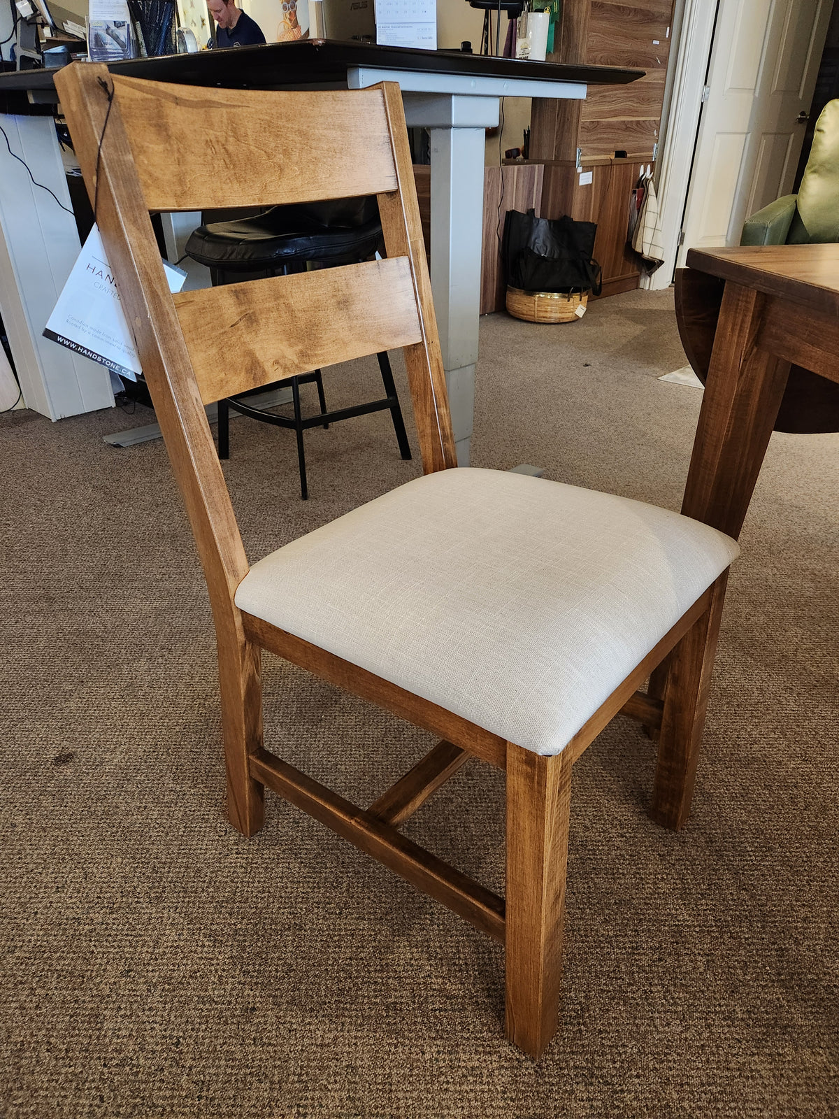 The wooden chair with light beige upholstery complements Handstone’s 3 Piece Parker Dining Table Set in a showroom.
