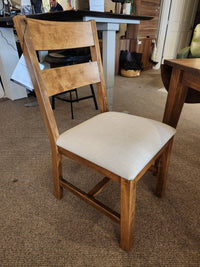 The wooden chair with light beige upholstery complements Handstone’s 3 Piece Parker Dining Table Set in a showroom.
