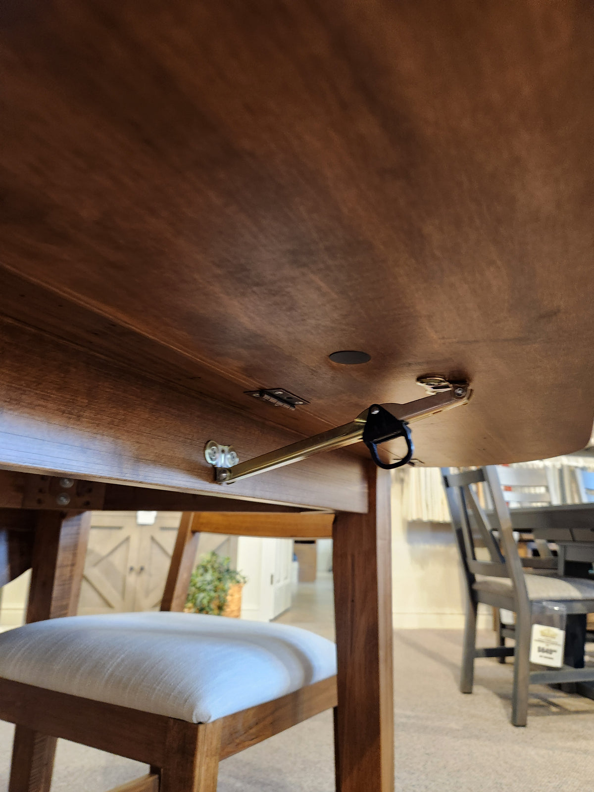 Underside view of Handstone 3 Piece Parker Dining Table Set with metal support hinge and cushioned chair underneath.