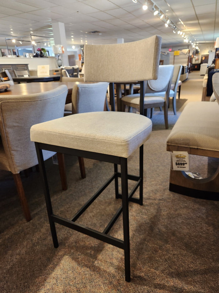 The Amisco Lucas Non Swivel Bar Stool features a beige seat and black metal frame, perfect for stylish showrooms.