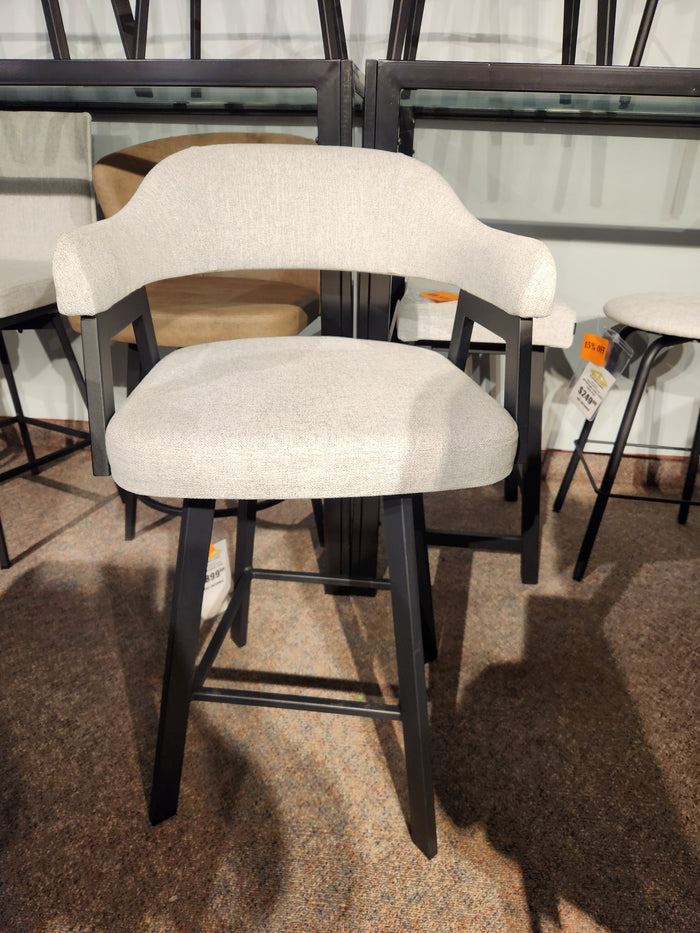 The Amisco Carmen Swivel Bar Stool features a light gray Scandinavian design and black wooden legs, shown in a showroom.