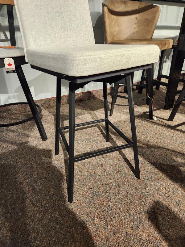The Dorian Swivel Bar Stool by Amisco features a beige cushion and black legs, shown on a brown carpet among other chairs.