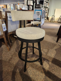 The Amisco Barry Swivel Bar Stool, beige with a black scratch-resistant finish, is on display in a furniture store.