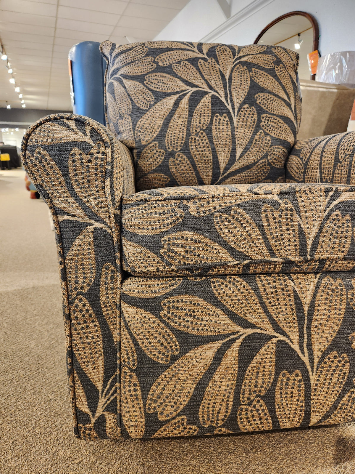 Best Kacey Swivel Glider Chair with beige and brown leaf pattern and reversible seat cushion, shown in store.