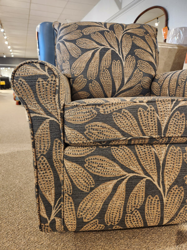 Best Kacey Swivel Glider Chair with beige and brown leaf pattern and reversible seat cushion, shown in store.