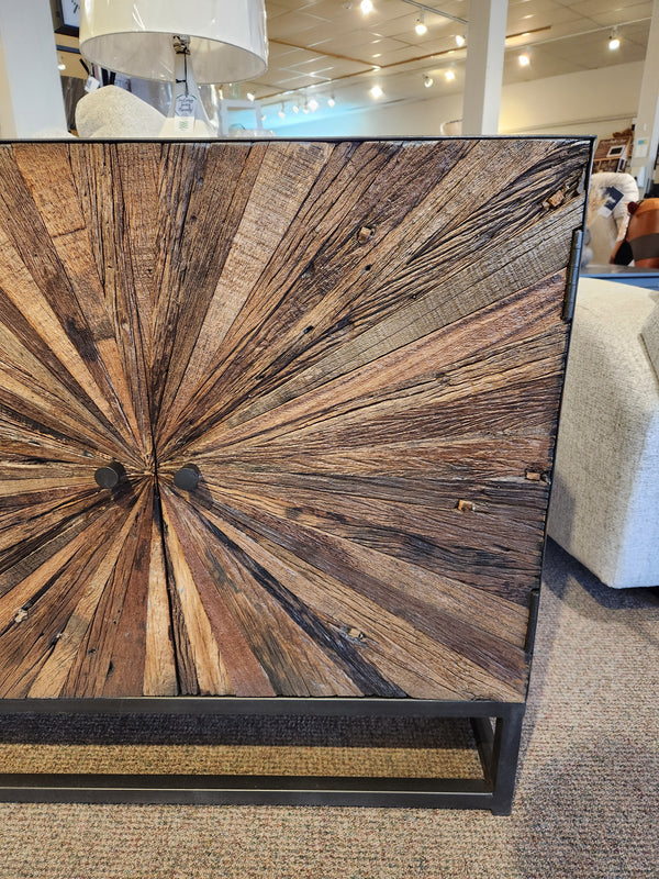 The Jofran 1928 Astral Plains 2 Door Cabinet features a starburst pattern and textured doors, displayed with other decor.
