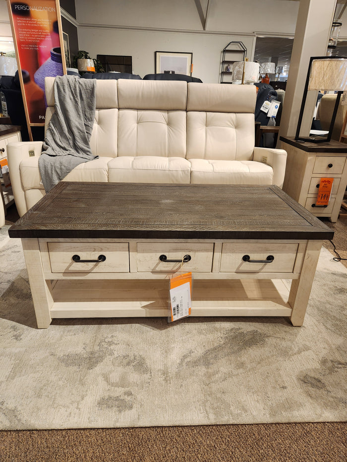 A beige sofa sits behind the Jofran 1706 Madison County Coffee Table, made of reclaimed pine with drawers.