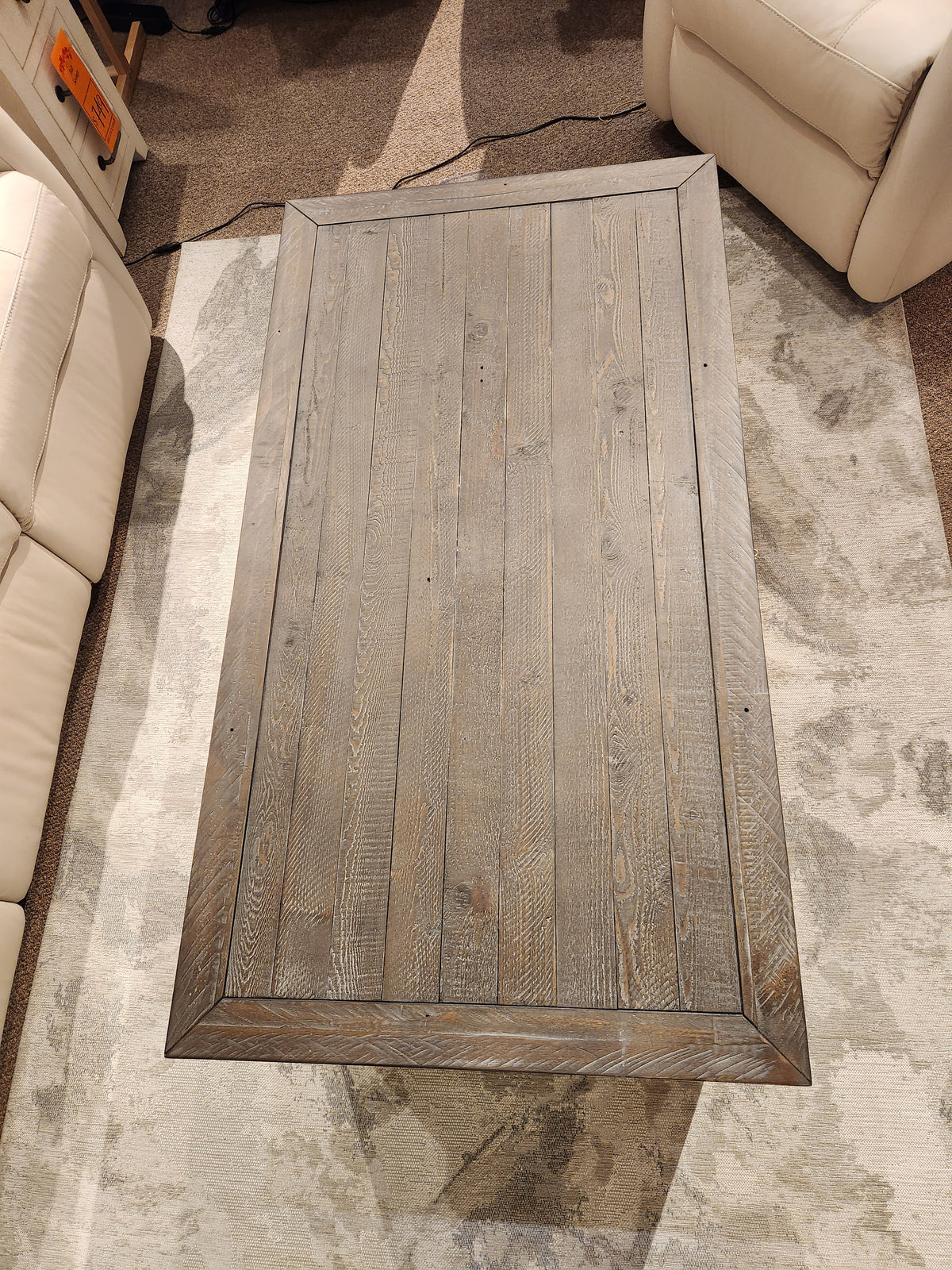 The Jofran 1706 Madison County Coffee Table sits among beige couches on a patterned rug.