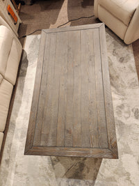 The Jofran 1706 Madison County Coffee Table sits among beige couches on a patterned rug.