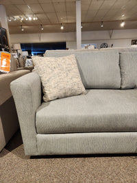 Decor-rest 2465 Queen Sofabed in gray upholstery with a textured beige pillow, shown in a showroom with overhead lighting.
