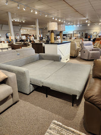 The Decor-rest 2465 Queen Sofabed is unfolded into a bed on the showroom floor with other Canadian upholstery on display.