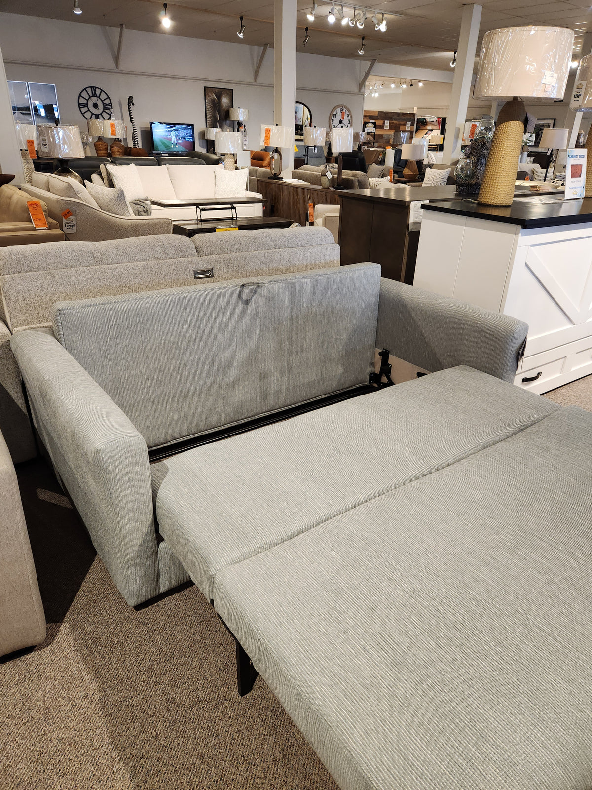 The Decor-rest 2465 Queen Sofabed in gray Canadian upholstery is shown extended in a furniture showroom.