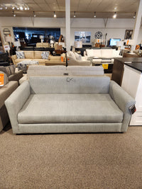 The Decor-rest 2465 Queen Sofabed, gray upholstered, is shown in a showroom with other couches and decor.