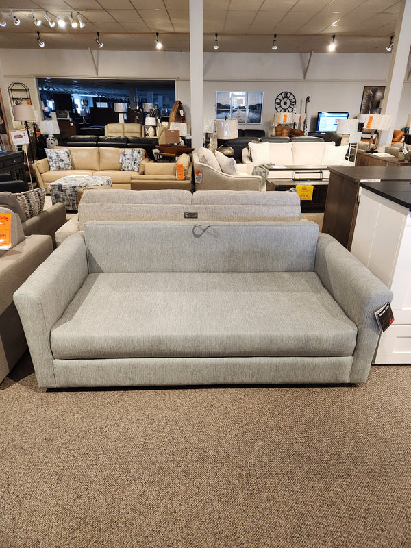 The Decor-rest 2465 Queen Sofabed, gray upholstered, is shown in a showroom with other couches and decor.