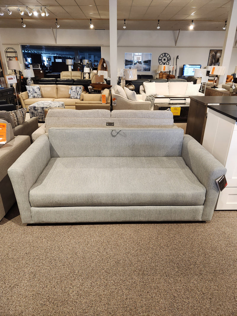 The Decor-rest 2465 Queen Sofabed, gray upholstered, is shown in a showroom with other couches and decor.