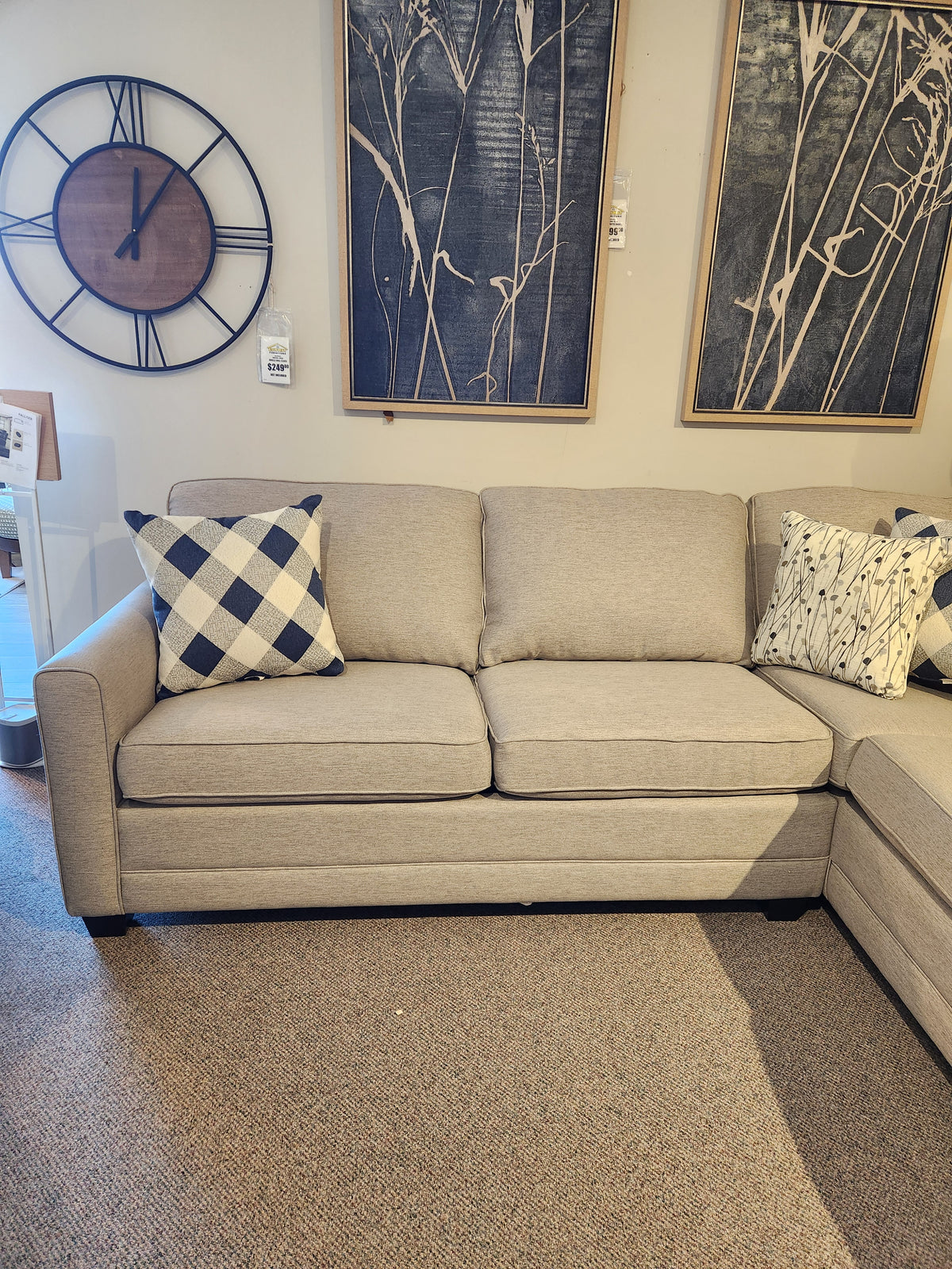 Beige 1014 Trinity Double Sofabed Sectional by Superstyle, with two patterned pillows, framed art, and a large round clock.
