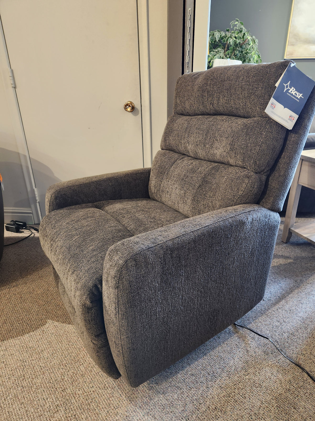 A gray Best 9NP34 Power Space Saver Recliner is on a carpeted floor near a closed door and side table.