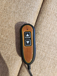 A two-button remote for the Golden Aurora PL480 Power Lift Chair rests on a beige upholstered surface.