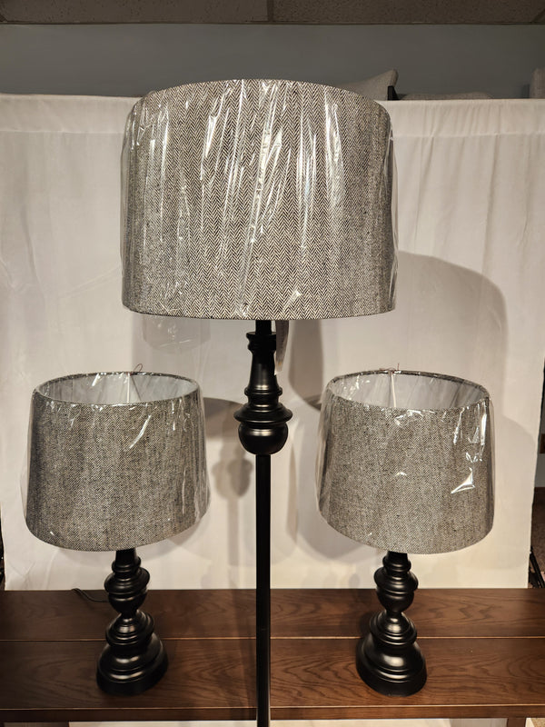 The Adesso Lamp Chandler 3 Piece Lamp Set features bronze table lamps with gray fabric shades on a wooden surface.