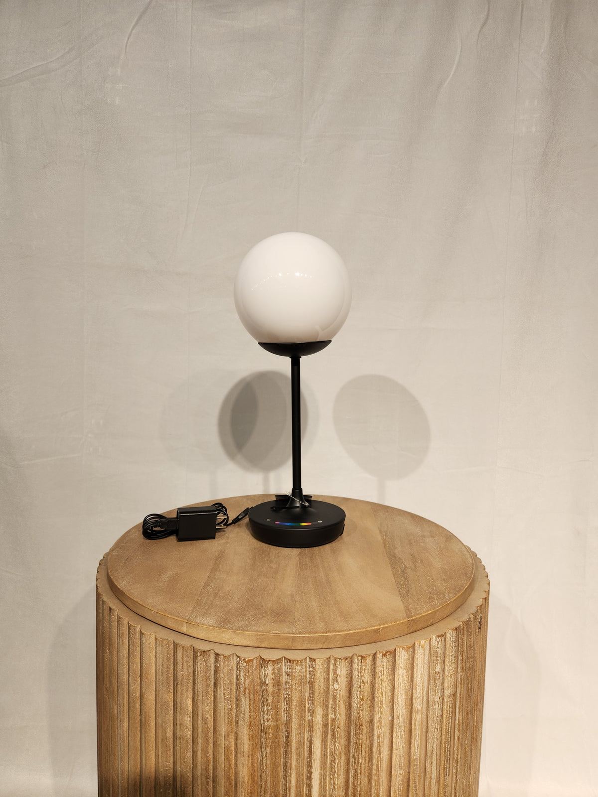 The Adesso Millie Color Changing Table Lamp with black base adds outdoor mood lighting on a wooden table.