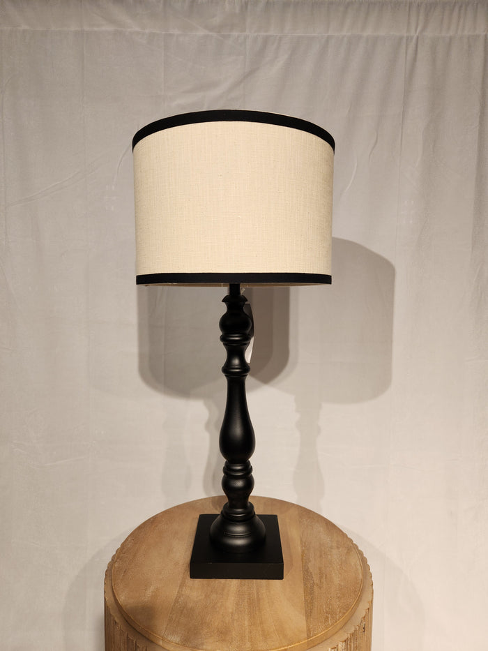 The Adesso Zeek Table Lamp sits on a round wooden table against a white curtain.