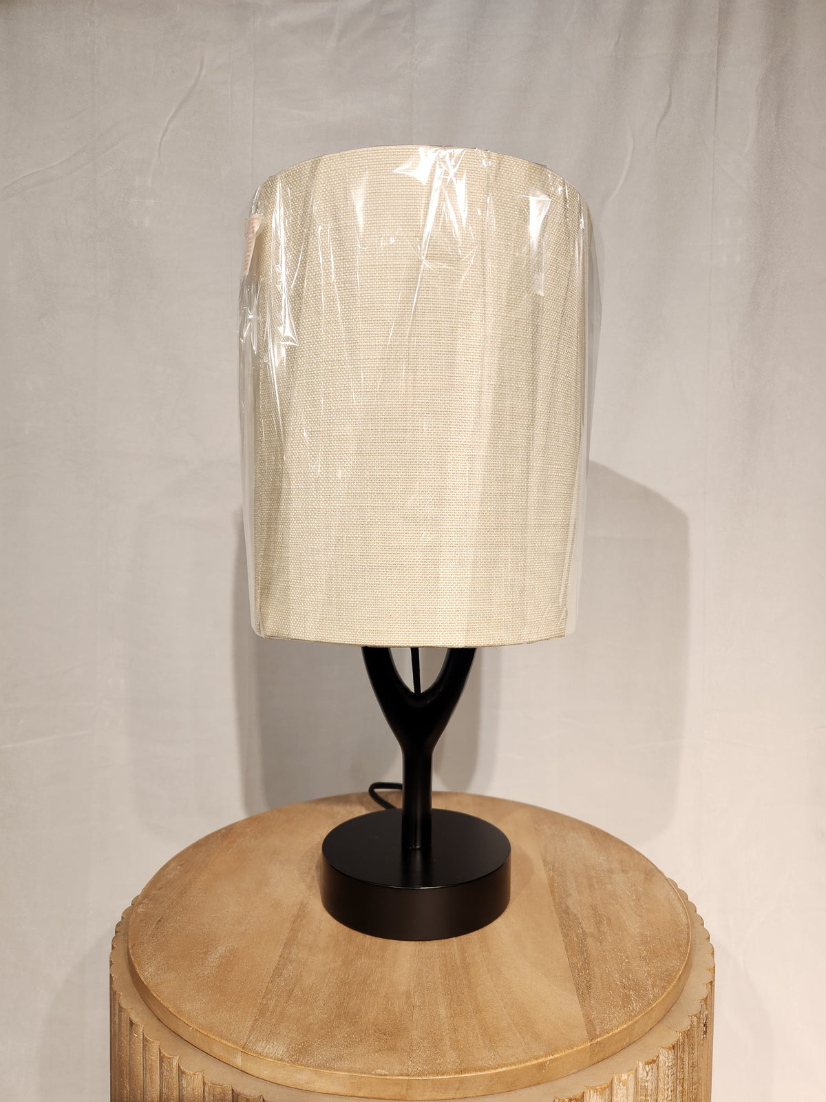 An Adesso Mayfair Table Lamp sits on a round wooden table, featuring a black wood base and beige shade.