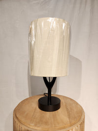 An Adesso Mayfair Table Lamp sits on a round wooden table, featuring a black wood base and beige shade.