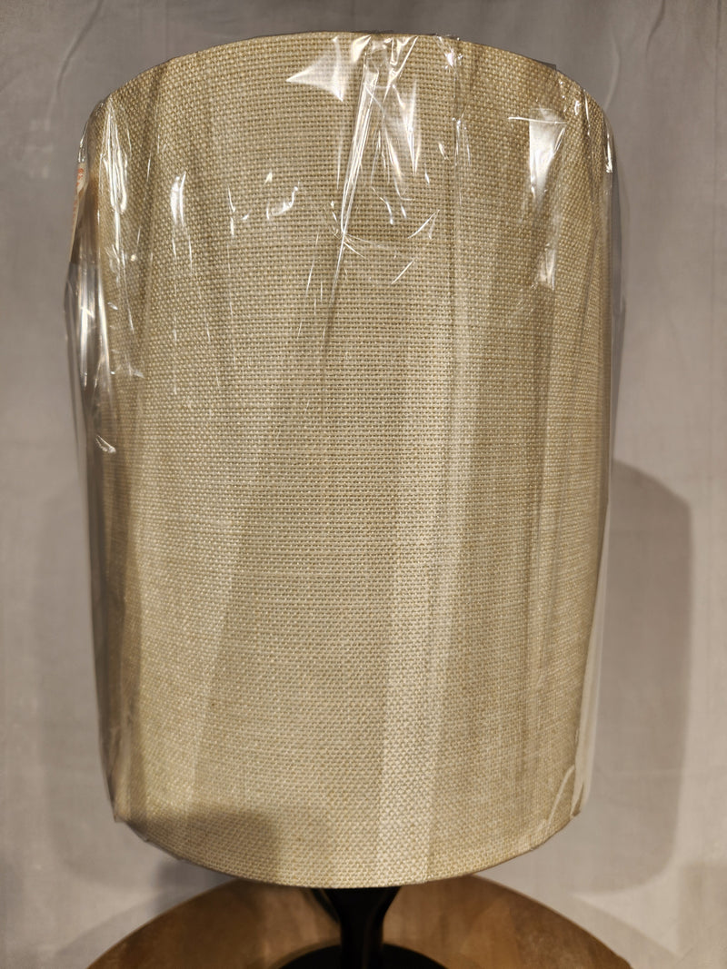 Beige fabric shade on a clear plastic and black wood Adesso Lamp Mayfair Table Lamp, set on a neutral background.