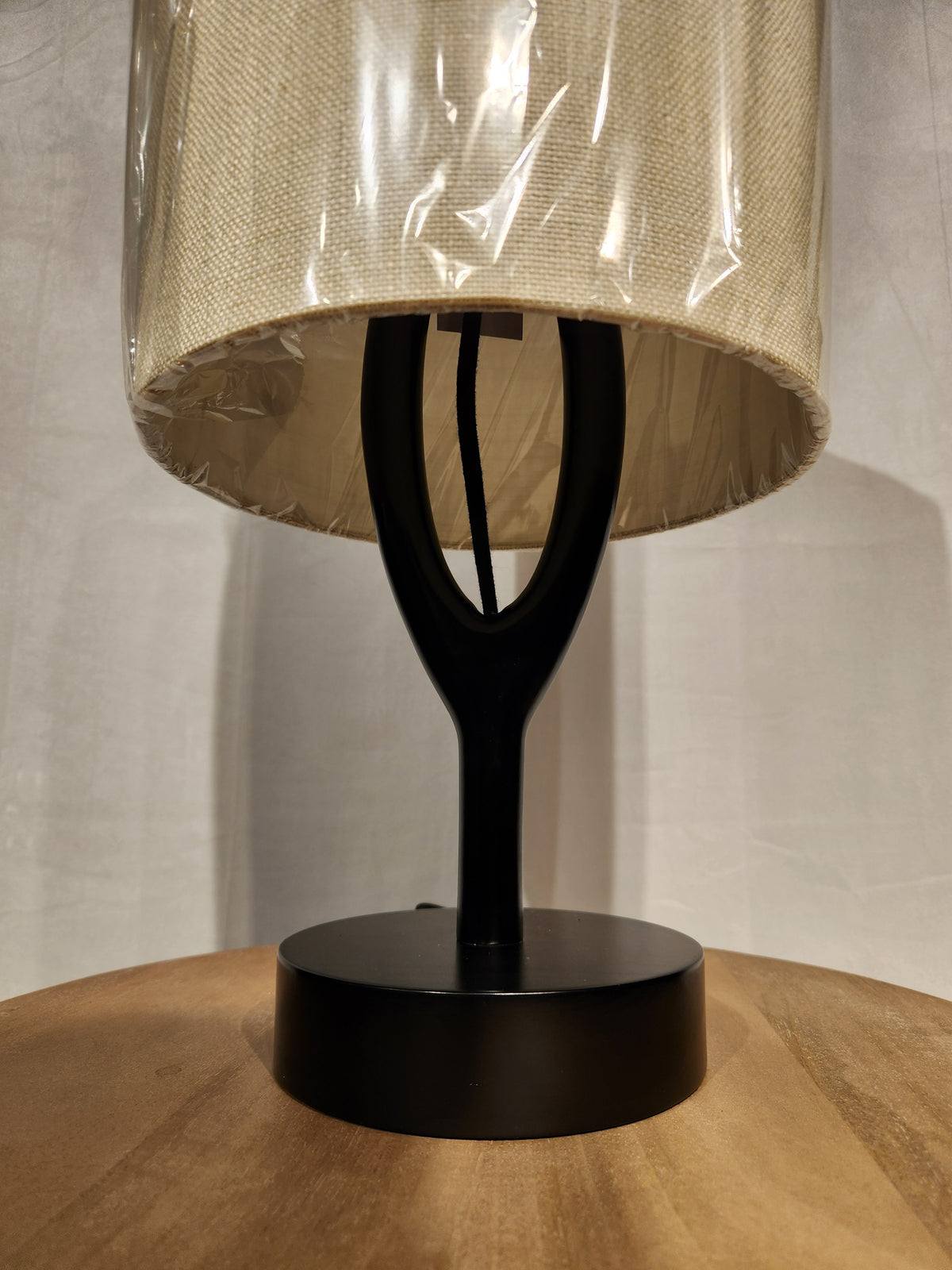 The Adesso Mayfair Table Lamp with a beige shade sits on a black wood surface, highlighting its modern design.