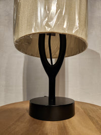 The Adesso Mayfair Table Lamp with a beige shade sits on a black wood surface, highlighting its modern design.