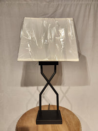 The Ashley Brookthrone Metal Table Lamp with a square shade rests on a round wooden surface.